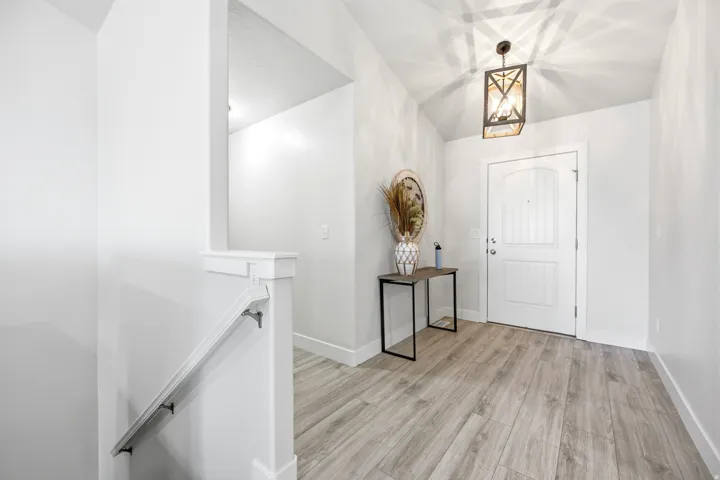 Vaulted ceiling with an industrial-style pendant light, wood-finish flooring, and white paneled entry door