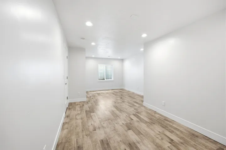 Recessed lighting illuminates the wood-finish flooring and light-toned walls