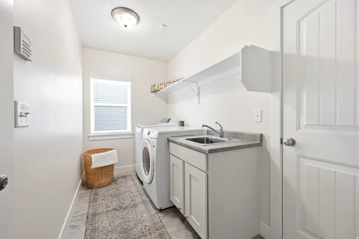 Laundry area featuring a utility sink, white cabinetry, and a window with blinds