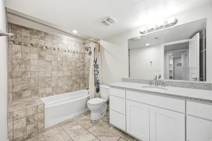 Full-height tiled shower surround with accent band, white bathtub, tile flooring, vanity with integrated sink, and large wall-mounted mirror