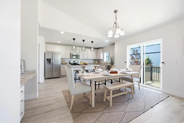 Open-concept living space with vaulted ceilings, wood-finish flooring, a kitchen featuring stainless steel appliances, and a sliding glass door leading to an outdoor patio