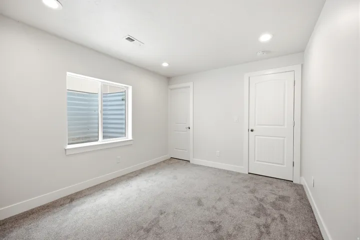 Recessed ceiling lighting, gray carpet flooring, white walls, and two white paneled doors with dark hardware