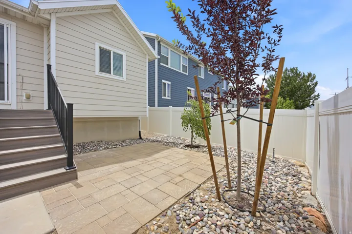 Paved patio area, composite deck stairs with black railing, light-colored horizontal siding, and full privacy fencing