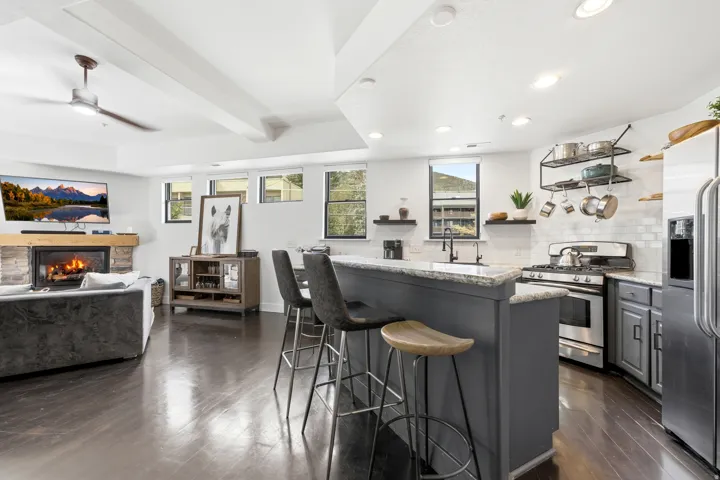 Open-concept living space featuring wood-finish flooring, a stone-surround fireplace, and an island with a light-toned countertop