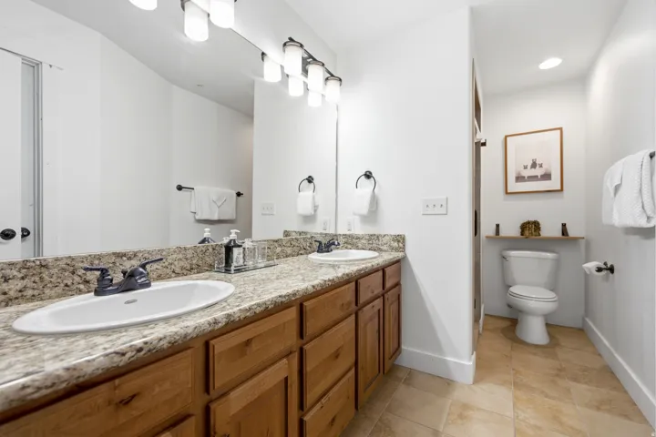 Dual vanity with granite-finish countertop, wood cabinetry, and matte black fixtures