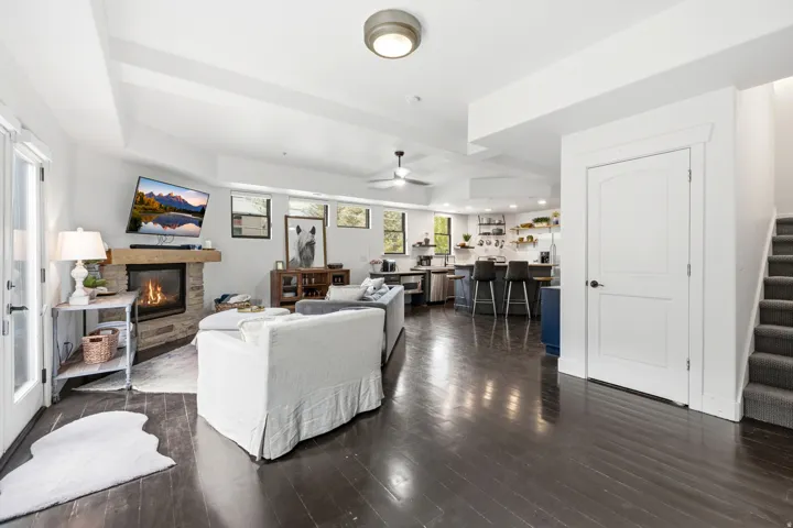 Spacious open-concept living area featuring dark wood-finish flooring, a stone-clad fireplace with a wood mantel, and an exposed beam ceiling