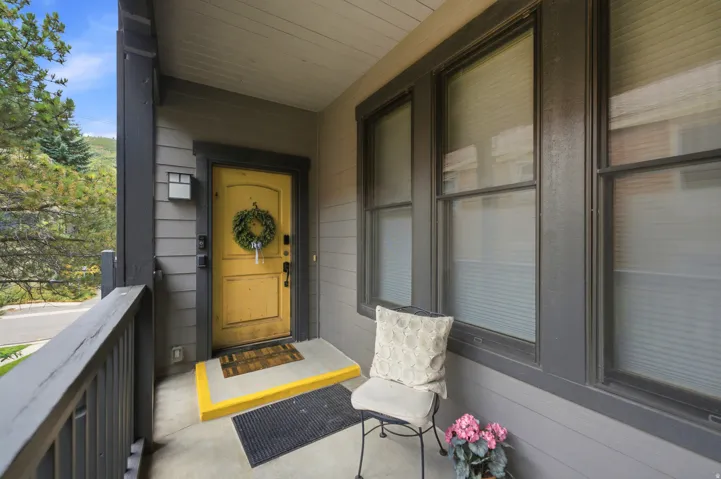 Covered porch entry featuring a yellow front door, exterior wall lantern, and multiple windows with blinds