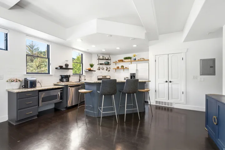 Open-concept kitchen with dark wood-finish flooring, white subway tile backsplash, stainless steel appliances, and a central island with bar seating