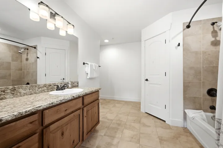 Bathroom featuring a double vanity with stone countertop, wood-finish cabinetry, and a combination shower/tub with tile surround