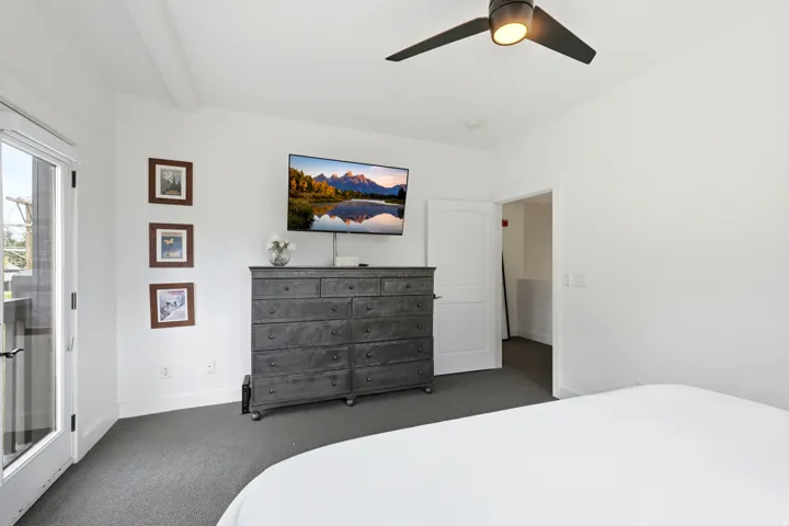 White interior walls, dark carpet flooring, and a ceiling fan with integrated lighting