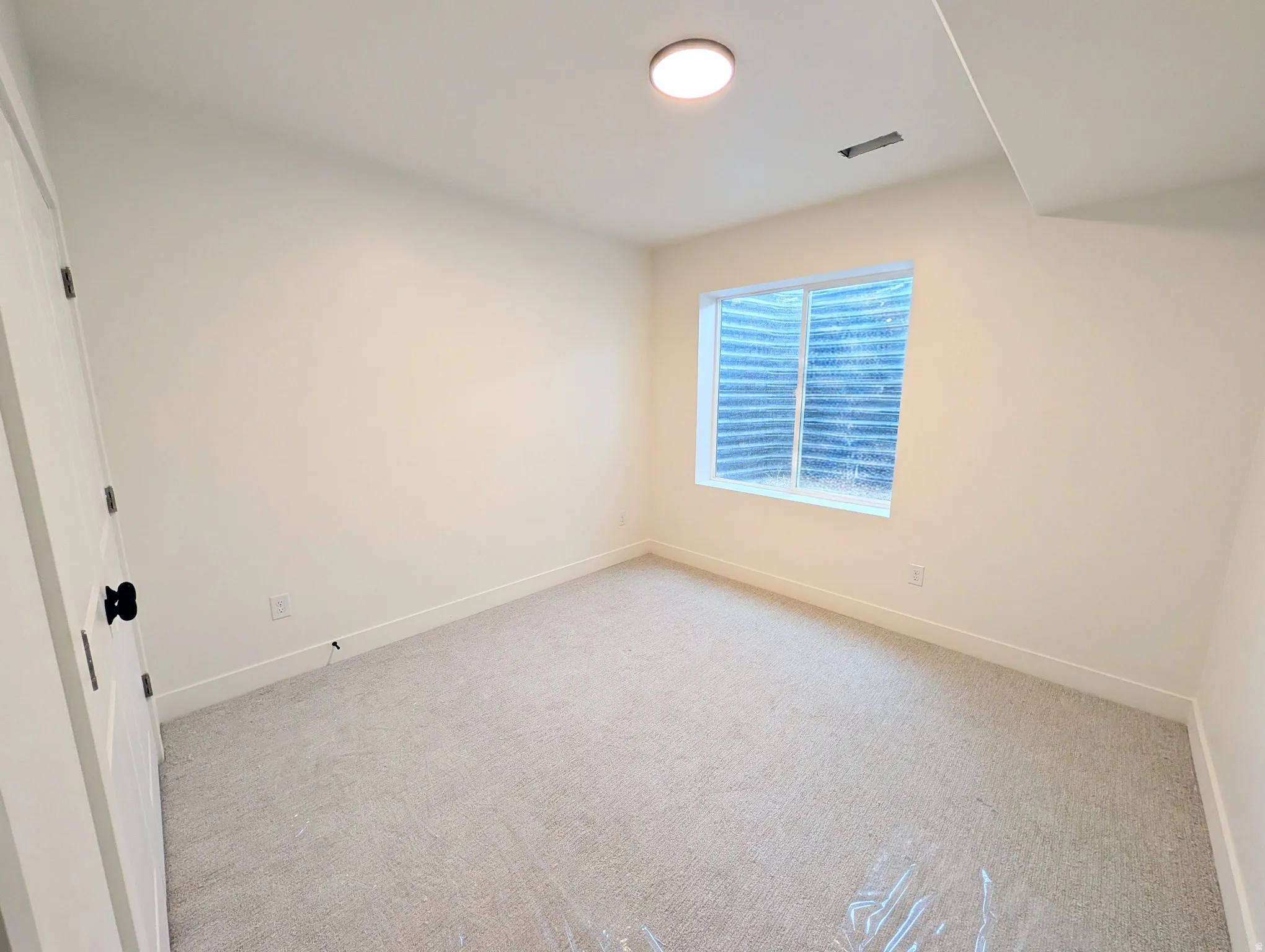 Bedroom #4-basement. Carpeted room with a window, recessed ceiling light, and white paneled door with a black knob