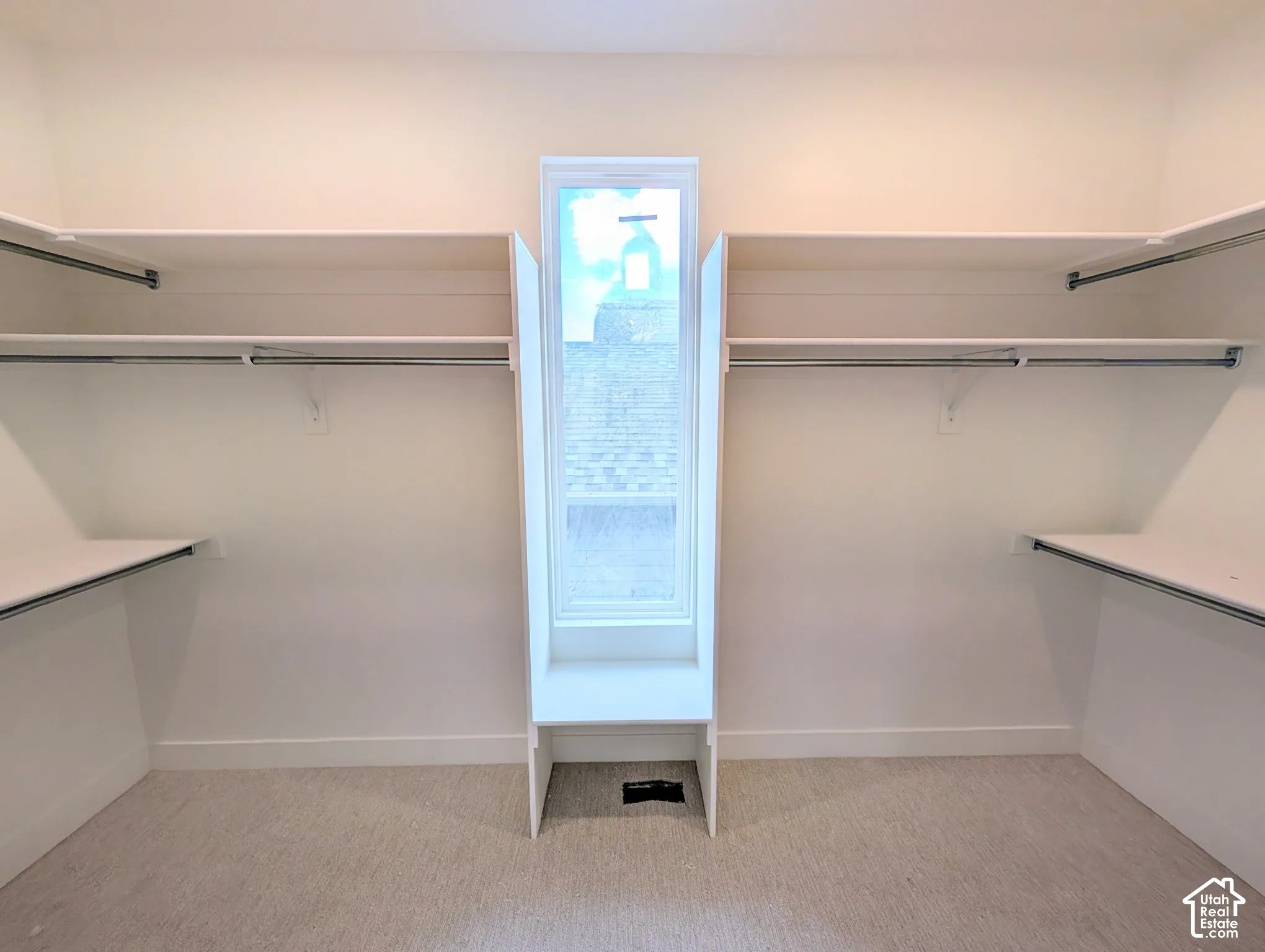 Walk-in closet with ample shelving and hanging rods, center window, and light-colored carpet flooring