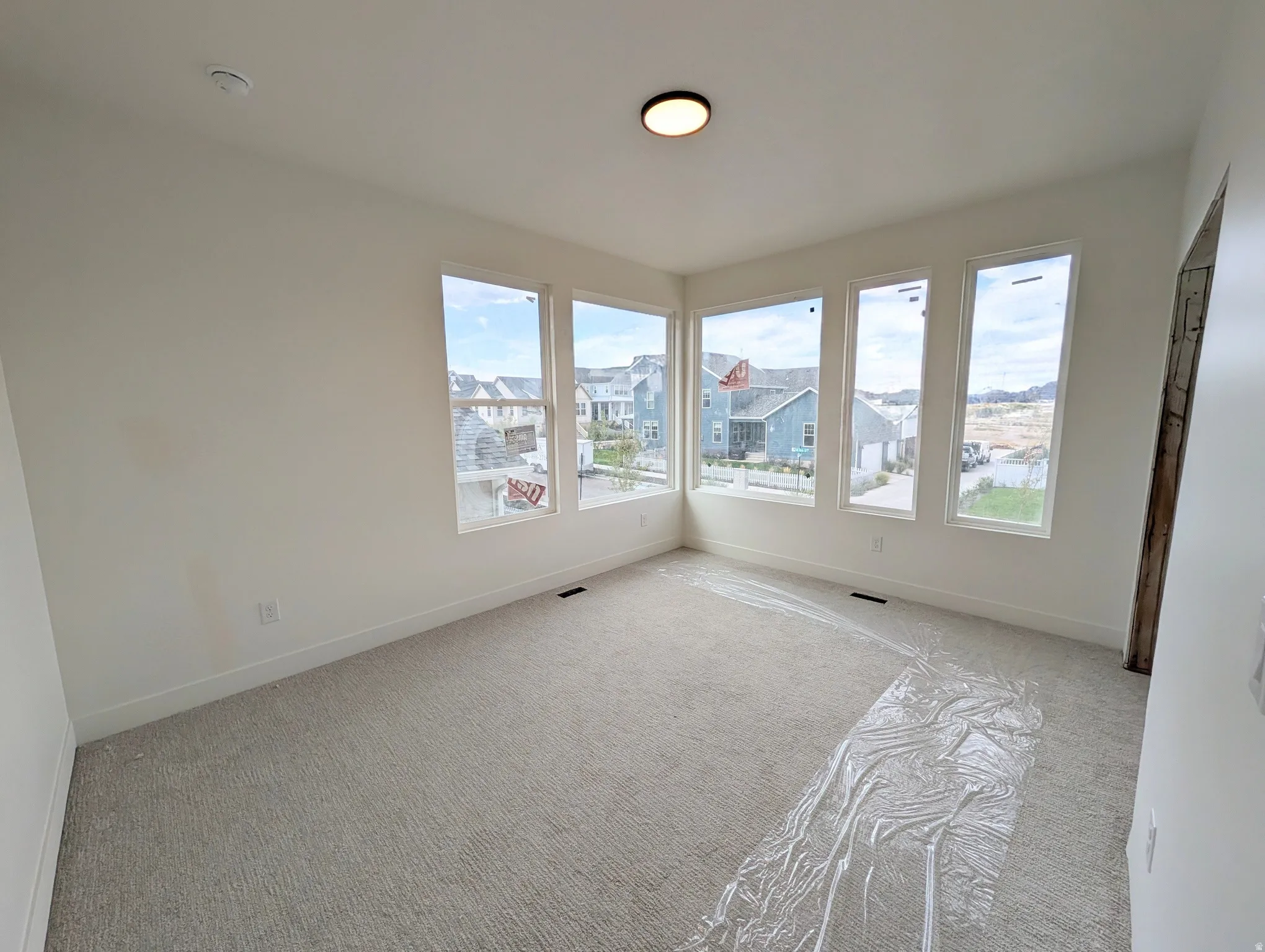 Bedroom #2. Expansive room featuring light neutral wall paint, gray carpet, multiple large windows, and a flush-mount ceiling light