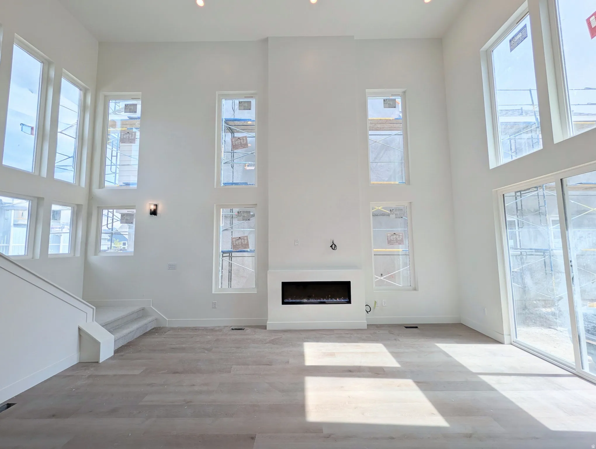 Soaring ceilings, multiple large windows, recessed lighting, integrated electric fireplace, and light wood-finish flooring