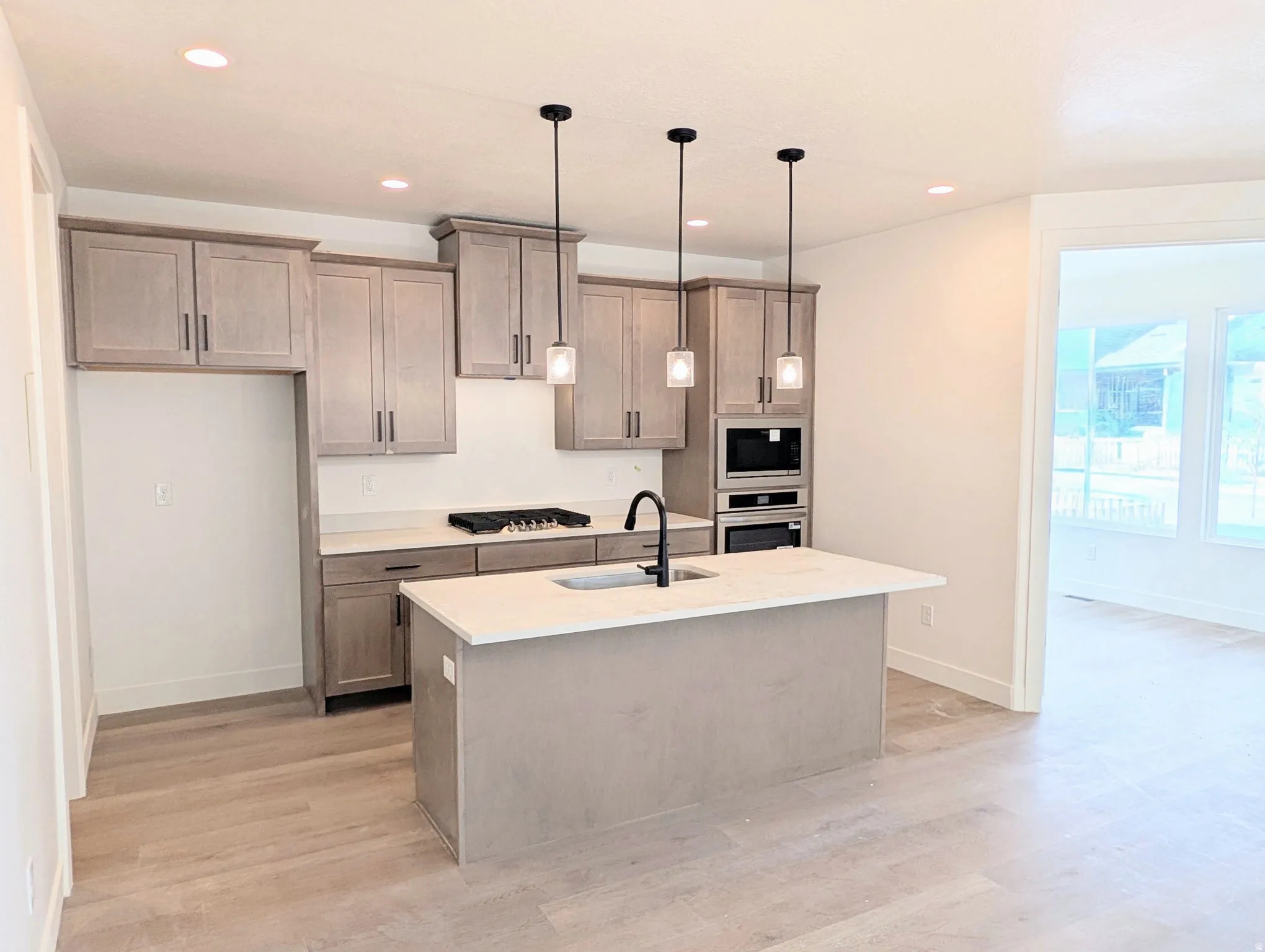 Kitchen featuring light wood-finish cabinetry, light countertops, wood-finish flooring, a central island with an integrated sink, and recessed lighting