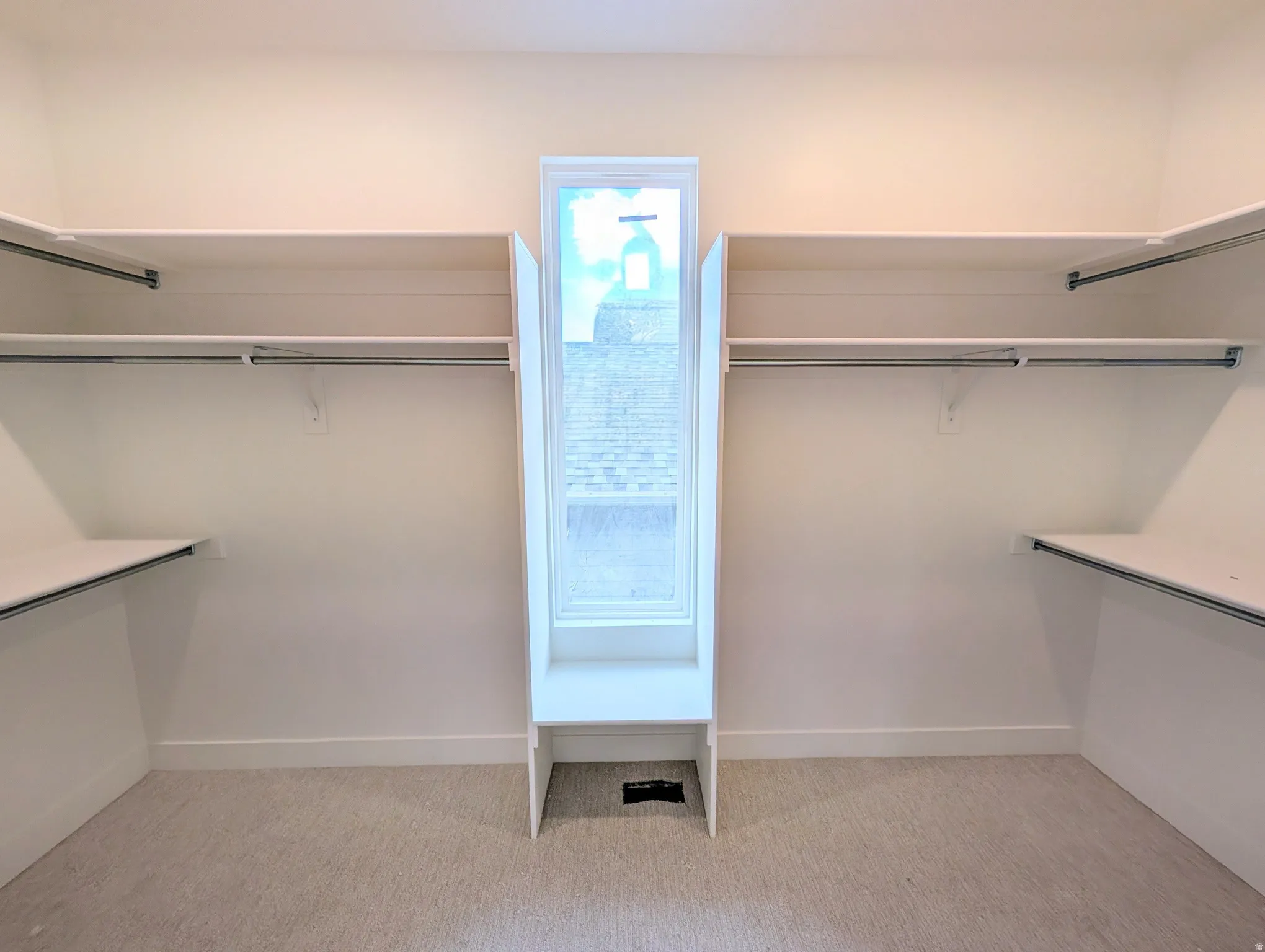 Walk-in closet with ample shelving and hanging rods, center window, and light-colored carpet flooring