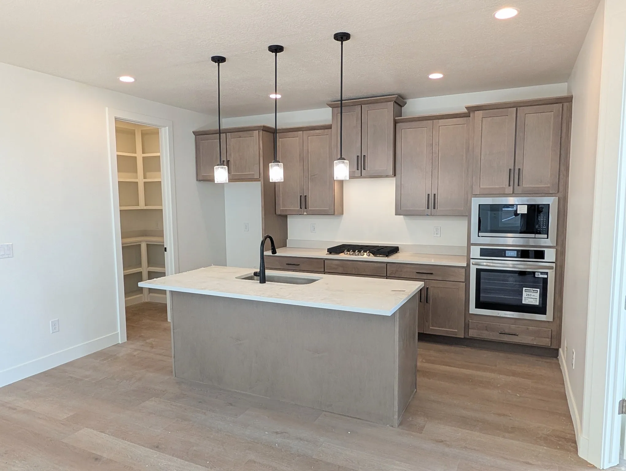 Kitchen featuring wood-finish cabinetry, stainless steel built-in appliances, a central island with a sink, pendant lighting, and wood-finish flooring
