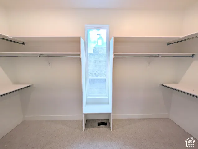 Walk-in closet with ample shelving and hanging rods, center window, and light-colored carpet flooring