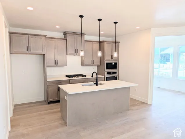 Kitchen featuring light wood-finish cabinetry, light countertops, wood-finish flooring, a central island with an integrated sink, and recessed lighting