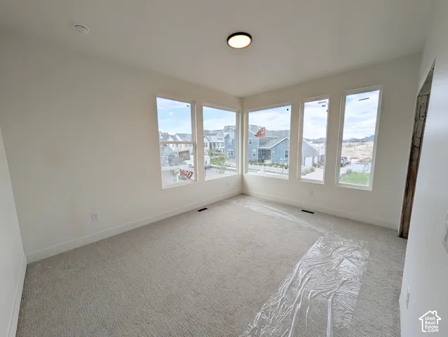 Bedroom #2. Expansive room featuring light neutral wall paint, gray carpet, multiple large windows, and a flush-mount ceiling light