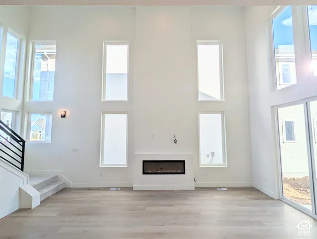 Double-height living space featuring expansive windows, wood-finish flooring, a contemporary electric fireplace, and a staircase with a black metal railing