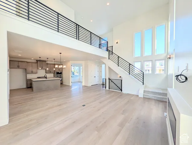 Double-height ceilings, wood-finish flooring, a contemporary staircase with horizontal railings, a modern kitchen with an island, and a built-in fireplace feature