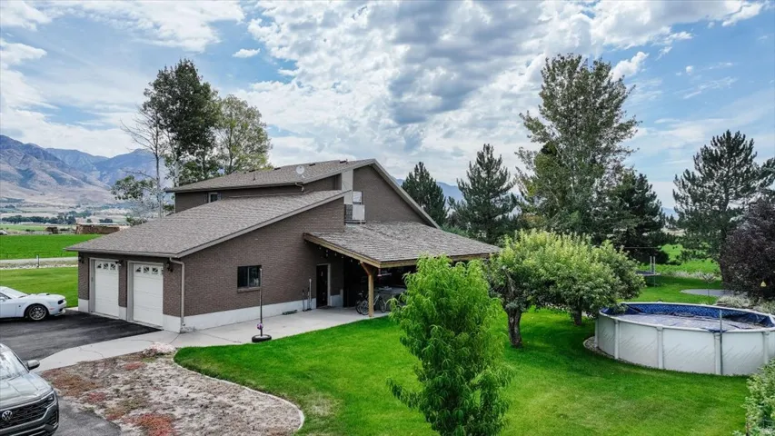 Two-car garage with white doors, covered carport, above-ground pool, and expansive green lawn
