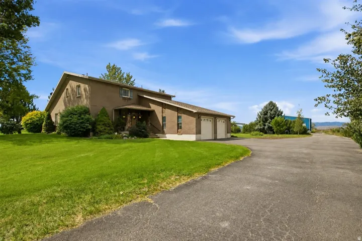 Brick exterior with a covered entry, attached two-car garage, expansive lawn, and paved driveway