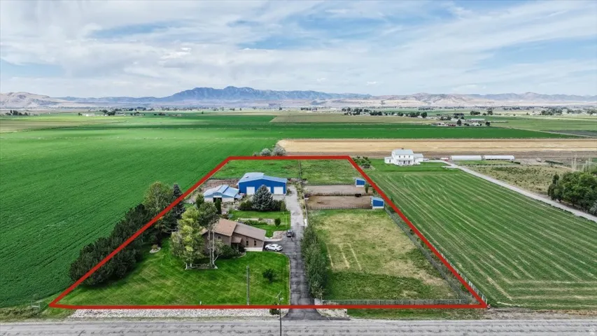 Expansive land parcel with surrounding agricultural fields, multiple outbuildings, and distant mountains