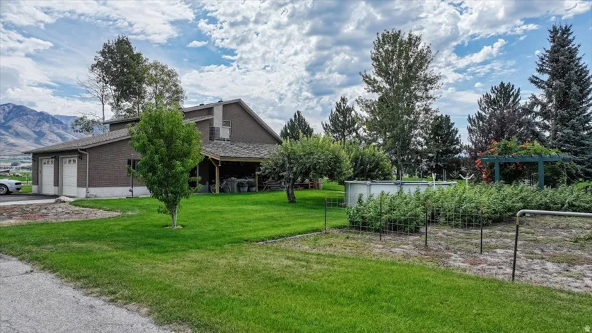 Two-car garage with white garage doors, covered patio, manicured lawn, garden with trellises, and mature trees