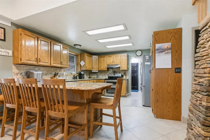 Kitchen featuring wood cabinetry, a center island with a granite-style countertop, a tile backsplash, and stainless steel appliances