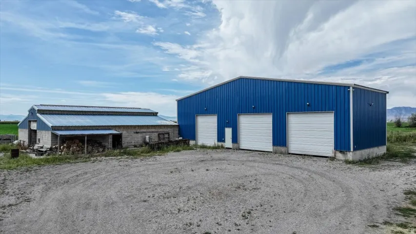 Versatile agricultural property featuring a classic barn structure with covered storage areas and a modern blue metal building with three overhead doors, ideal for equipment and operational needs