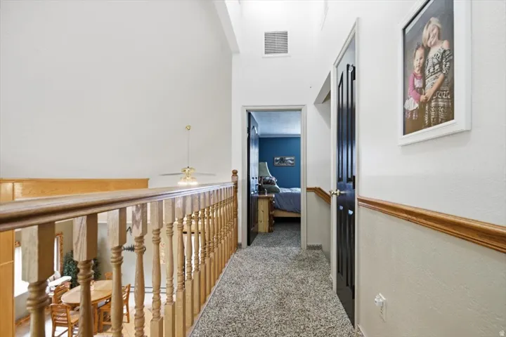 Carpeted hallway with wood railing and chair rail molding, vaulted ceiling, and a ceiling fan