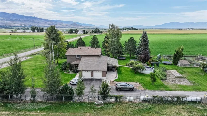 Two-story residence with a two-car garage, expansive green lawn, mature trees, and mountain backdrop