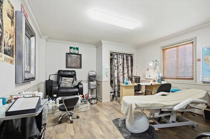 Room featuring wood-finish flooring, crown molding, chair rail paneling, and a window with blinds