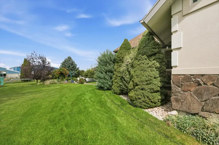 Expansive green lawn with mature evergreen trees and a stone-clad foundation