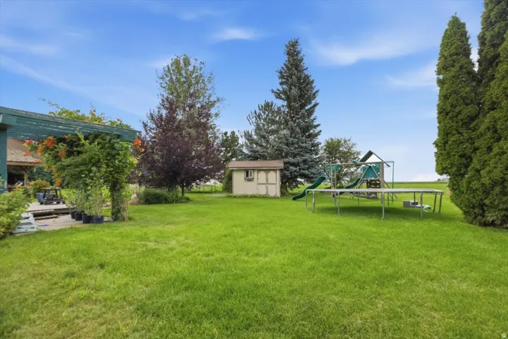 Expansive grassy yard featuring mature trees, a detached storage shed, and a wooden deck with an overhead pergola