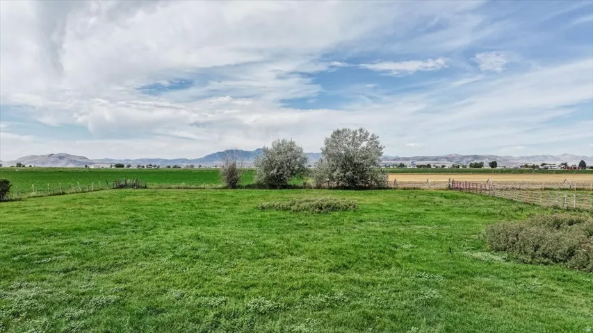 Expansive green field with natural landscaping, distant mountains, and partially cloudy skies