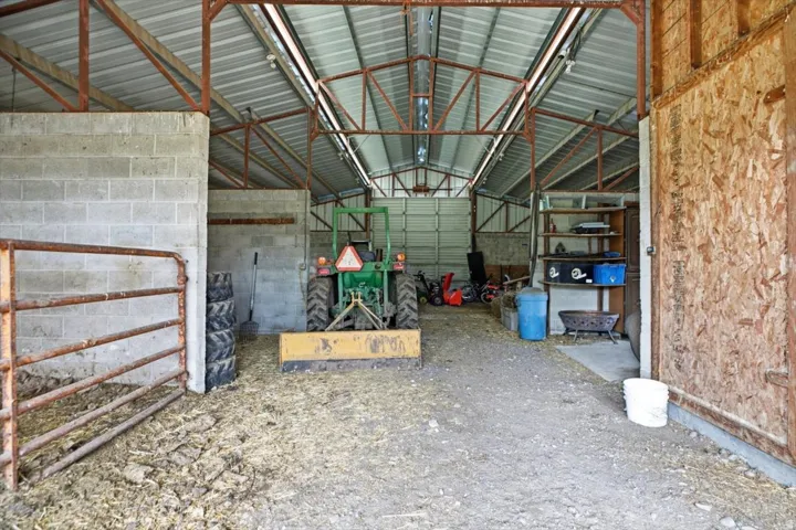 Open-span barn structure featuring a metal roof, exposed truss system, concrete block wall, and integrated shelving
