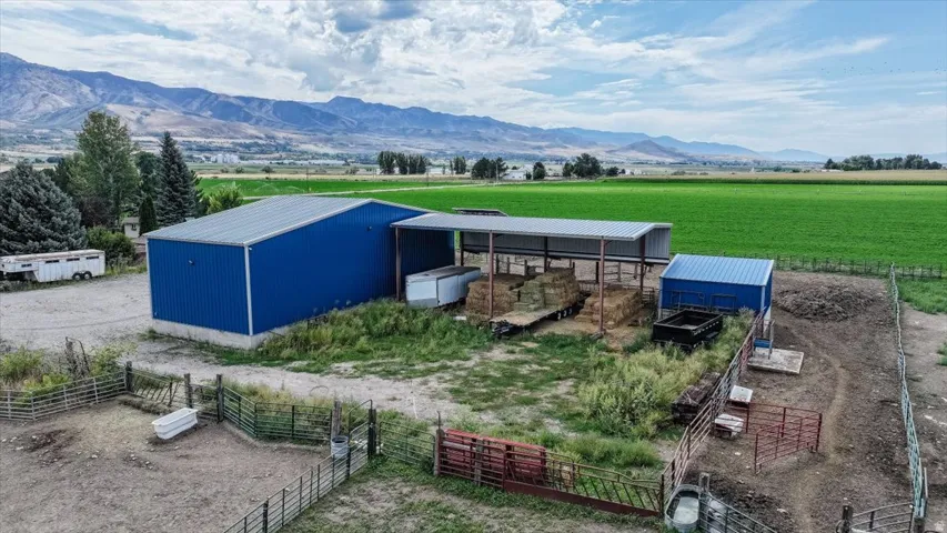 Blue metal-sided barn structure featuring an attached covered open-air storage area, a separate blue metal-sided outbuilding, and fenced enclosures