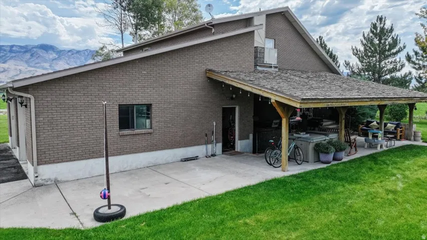 Brick exterior with a covered patio, concrete paving, and an expansive lawn