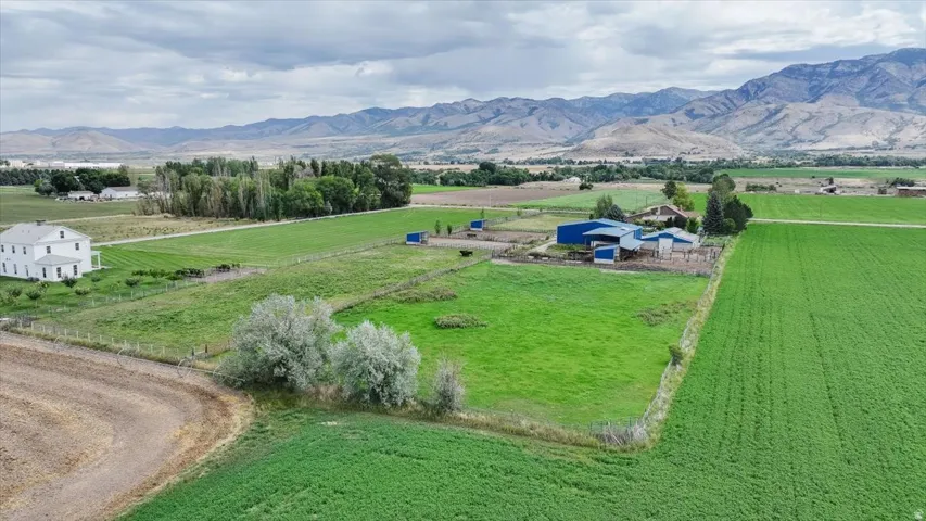 Expansive agricultural property featuring a white two-story residence, multiple outbuildings with blue roofs, fenced pasture, and cultivated fields