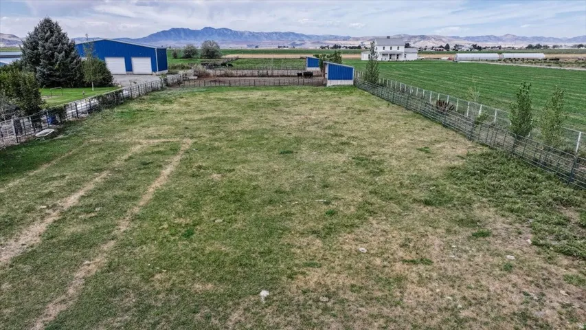 Expansive grass area with metal fencing, bordered by a large blue outbuilding with two white garage doors, and distant mountains