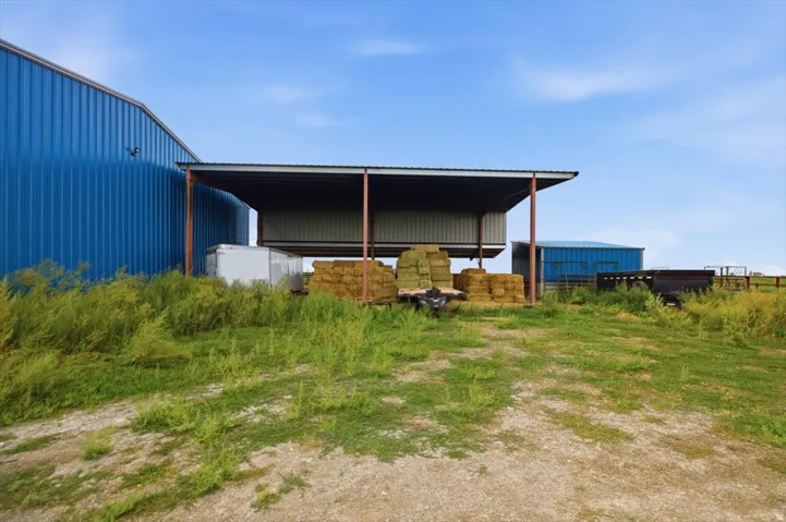 Corrugated metal barn with an attached covered shelter, featuring a gravel and grass foreground