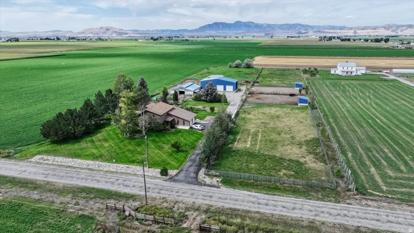 Property featuring a single-story residence, a detached garage, multiple outbuildings, fenced enclosures, and expansive surrounding fields