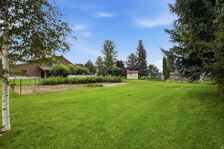 Expansive lawn area with mature trees, a detached storage shed, and a privacy fence