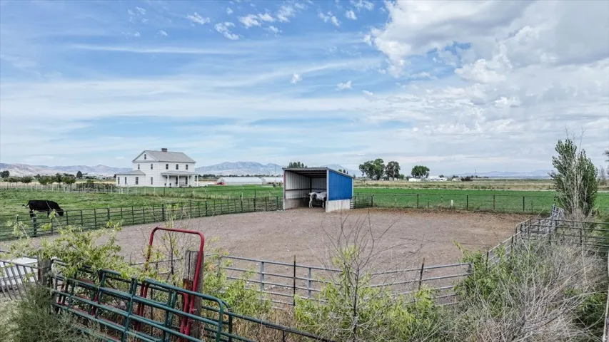 Expansive property featuring a white two-story residence, metal fencing, a large turnout paddock, and a blue-roofed shelter