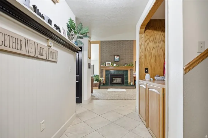 Tiled flooring, built-in wooden cabinetry, wooden staircase with railing, brick fireplace with mantel, and green tile surround