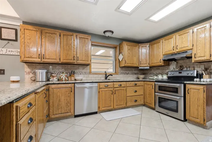 Kitchen featuring wood cabinetry, light-toned countertops, a tile backsplash, stainless steel appliances, and ceiling-mounted lighting