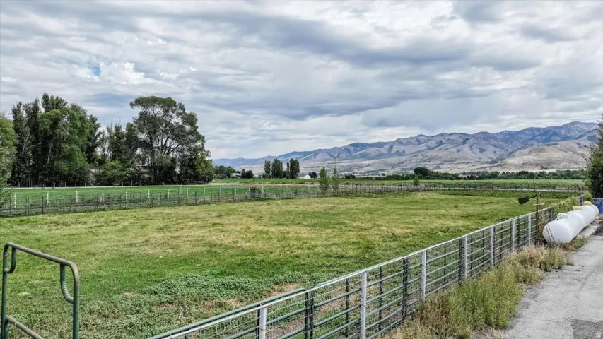 Expansive green field with perimeter fencing, mature trees, and mountainous backdrop